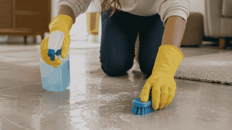A dog owner wearing rubber gloves thoroughly cleaning and disinfecting a floor surface with diluted bleach solution after parvo exposure, showing the correct decontamination procedure to eliminate parvovirus from the home environment