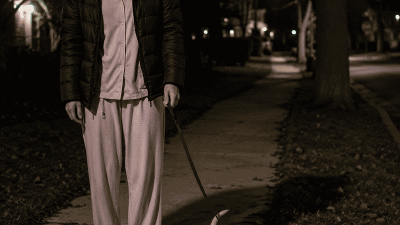 A tired dog owner standing outside late at night with her young puppy during an overnight potty training trip, showing the reality of the early weeks of how to potty train a puppy